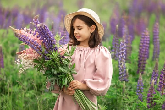 Young caucasian girl in hat holding lupines in blooming field.