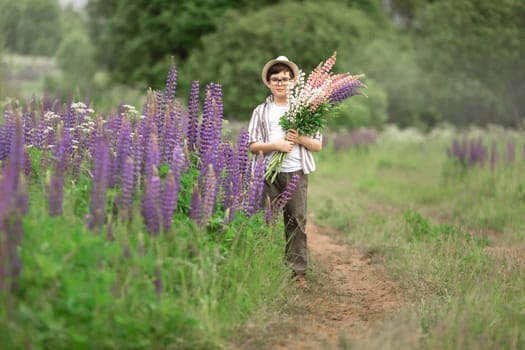 Young caucasian boy holding lupine flowers in lush green field.