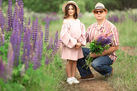 Young caucasian girl and mature caucasian man in flower field with hat and purple lupines.
