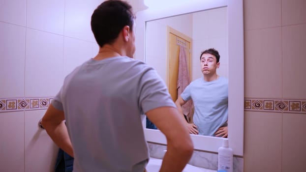 Tired man looking at his reflection in the bathroom mirror before going to work, feeling sleepy and unmotivated