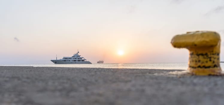 Luxury boat moored off pier on Kos coastline with Blue Star Ferry in background and defocused yellow bollard in foreground