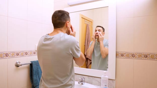 Caucasian man applying eye patches for beauty treatment in front of bathroom mirror