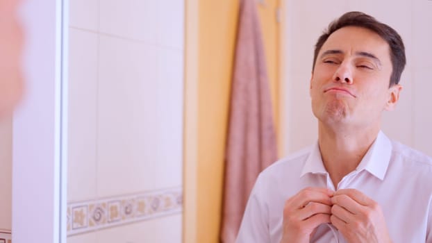 Successful businessman getting dressed, buttoning his white shirt in the bathroom, feeling confident and ready for the day