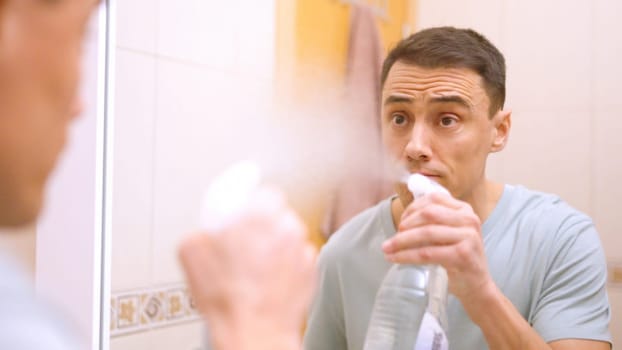Man spraying cleaning product on bathroom mirror, preparing to wipe and polish
