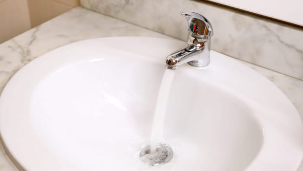 Stream of fresh water running from a faucet into a white sink in a clean bathroom. Concept Wasting water