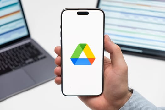 PRAGUE, CZECHIA - JULY, 2024: Google disk logo on the screen of smartphone in mans hand and laptop on the background