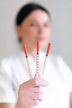 Female cosmetologist holding injection syringes in clinic. Young skin therapist is wearing pink glove and uniform in beauty spa salon