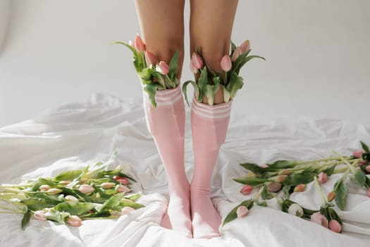 Legs in pink socks filled with fresh tulips on a white bed, playful floral fashion concept, soft natural light aesthetic.