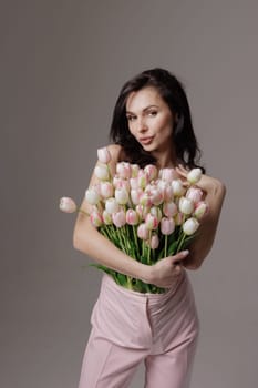 Elegant woman holding a bouquet of pink and white tulips, stylish fashion concept with flowers tucked into trousers, romantic and modern aesthetic