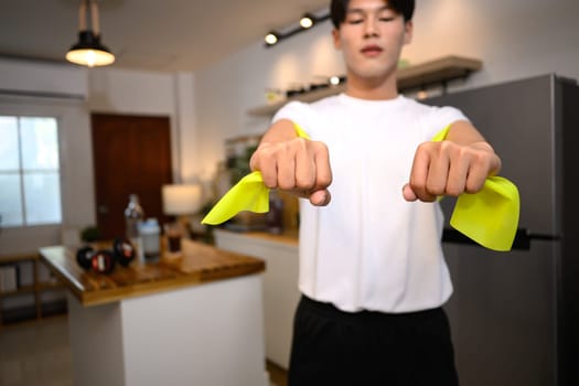 Close up of young man exercising with resistance band in cozy home.