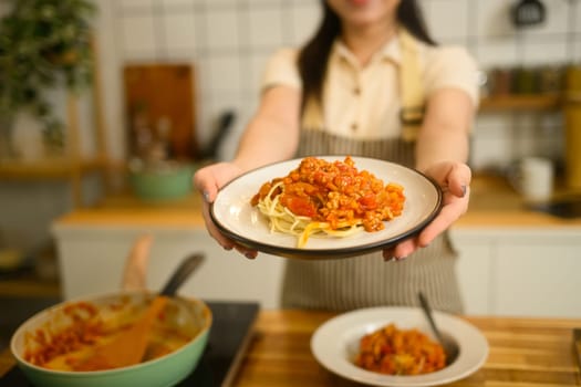 Close up woman proudly holding a plate of homemade spaghetti, ready to be served.