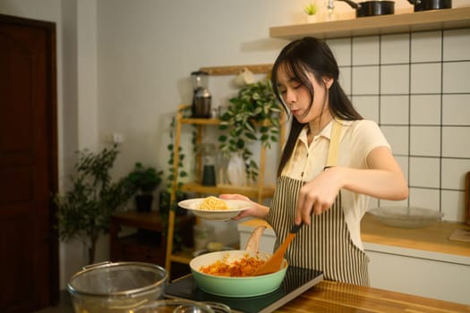 Asian woman stirring rich tomato based sauce on the stove while getting ready to serve freshly prepared pasta dish.