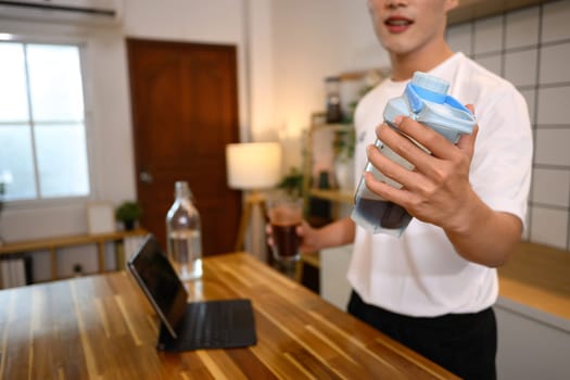 Man in white sports shirt preparing a protein shake in a stylish kitchen.