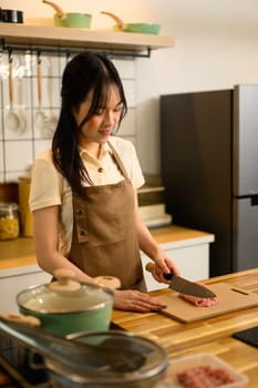 Young woman wearing a brown apron preparing Ingredients for spaghetti in a kitchen.