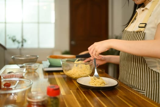 Young woman twirls a forkful of spaghetti onto a plate, getting ready to serve a delicious homemade meal.