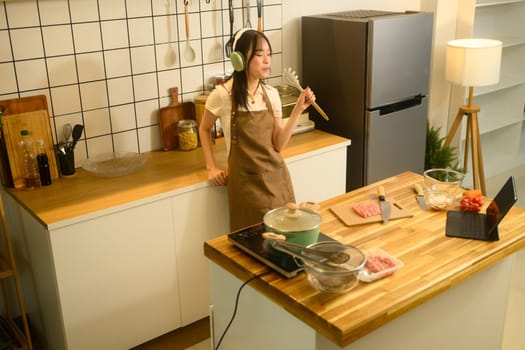 Young woman dancing and singing while preparing spaghetti in a cozy kitchen.