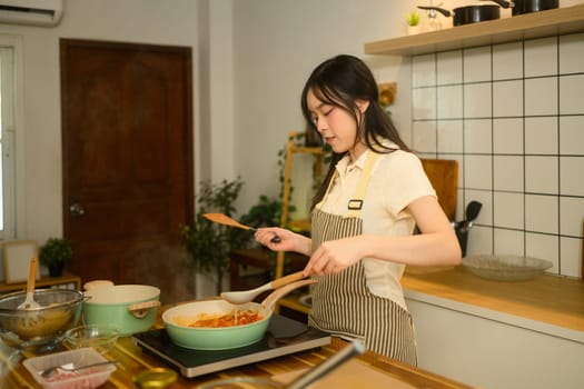 Young woman in apron preparing spaghetti sauce in cozy kitchen.