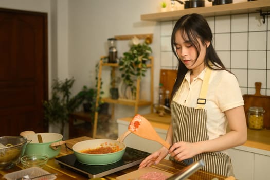 Young woman in apron preparing spaghetti sauce in cozy kitchen.