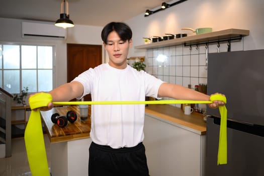 Young asian man exercising with a resistance band in a stylish kitchen.