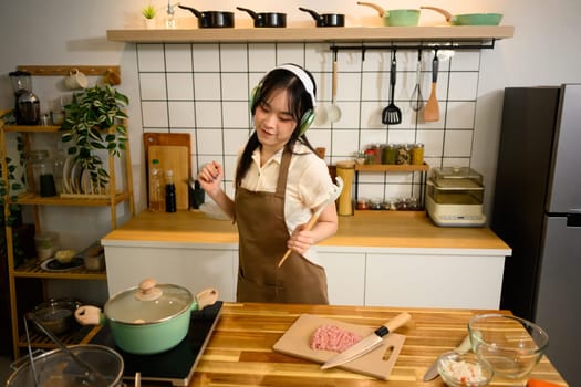 Joyful young woman listening to music through headphones and dancing in the kitchen.