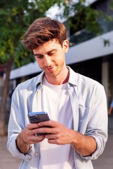 smiling man using his cell phone while walking down the street, he is wearing a white shirt and is focused on his phone, concept of technology of communication and urban lifestyle, copyspace for text
