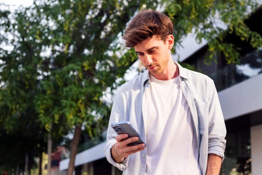man using his cell phone while walking down the street, he is wearing a white shirt and is focused on his phone, concept of technology of communication and urban lifestyle, copyspace for text