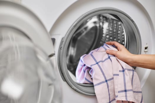 female hand putting color cotton clothes into the washing machine, close-up