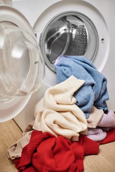 Colorful and white wool laundry and washing machine with open door. Close up.