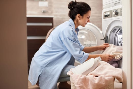 woman put pastel cotton towel in automatic washing machine with open door in bathroom