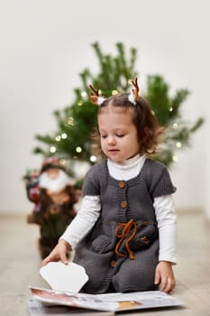 Cute little child girl reads a book near the Christmas tree at home