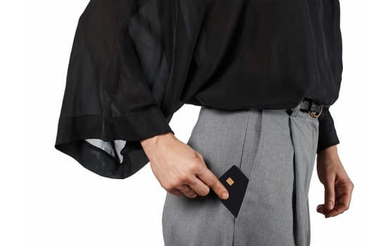 Modern business woman putting black premium credit bank card in grey pants pocket on white background. Money finance