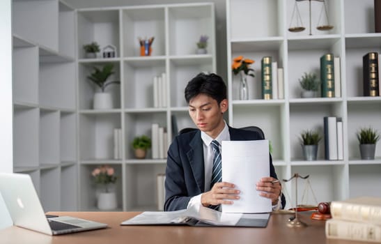 A young professional dressed in a suit is carefully examining documents at his desk, focused on analysis and decision-making in a sleek office setting.