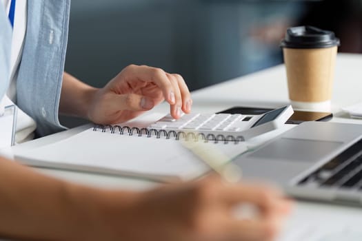 A person calculates financial data using a calculator and notes, showcasing a blend of technology and traditional methods in a work setting.