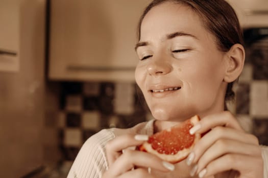 Woman savoring the taste of a juicy grapefruit in her kitchen. Eyes closed, face expressing pure enjoyment.