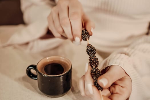 Close-up of hands delicately arranging small dark objects onto a twig-like structure beside a dark mug of coffee.