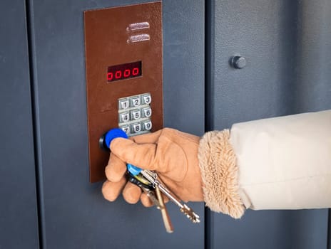 Woman in a warm cloth and gloves opening the electronic lock with the chip on the key chain