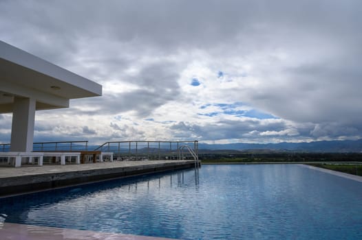 Clouds gather over a tranquil poolside retreat, reflecting scenic mountains and vast landscapes in the distance.