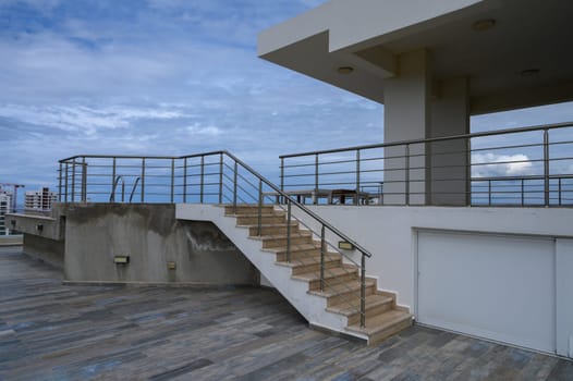 Stairs lead to a stylish rooftop terrace surrounded by coastal views and modern architecture, under blue skies.