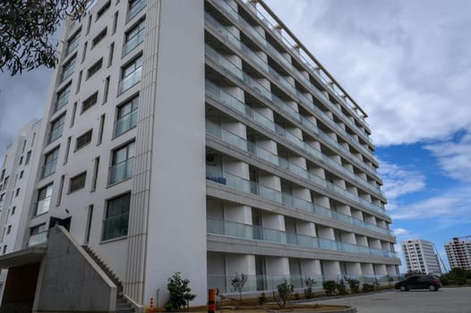 A modern building rises under a cloudy sky, showcasing balconies and minimalist design for urban living.