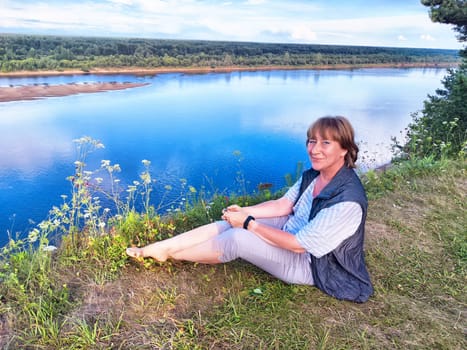 A middle-aged female traveler blogger captures a selfie by a serene river, surrounded by lush greenery.