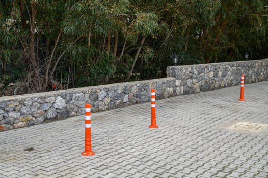 Orange traffic cones form a clear boundary in a tranquil parking area surrounded by lush greenery and a stone wall.