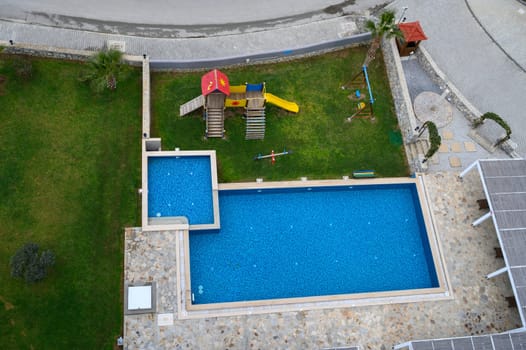 Vibrant blue waters enhance a tranquil pool area featuring a fun playground surrounded by lush green grass.