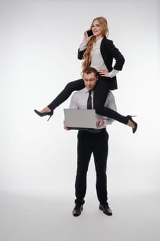 A couple enjoys a fun activity, with one balancing on the other's shoulders while using a laptop.