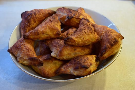 A bowl filled with several pieces of triangular, golden-brown pastries. The pastries appear to be well-baked with a flaky texture, likely indicating that they are made from puff pastry