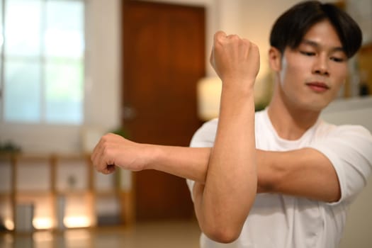 Young asian man sitting on floor stretching his arms while working out at home.
