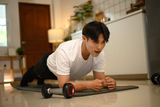 Young Asian man doing plank exercise on yoga mat at home.