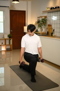 Full length of young man exercising with dumbbells in a lunge position at home.