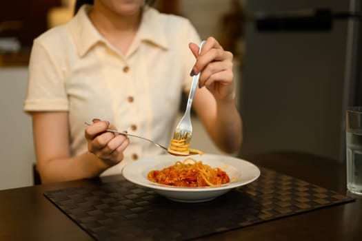 Close up of woman twirling spaghetti with fork while enjoying a homemade meal in a kitchen.