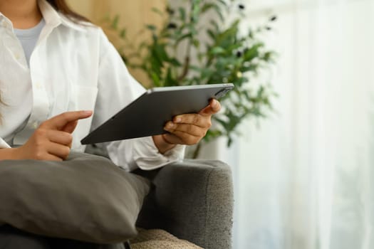 Cropped shot of female freelancer using a digital tablet while sitting on a comfortable couch.