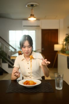 Asian woman enjoying a homemade spaghetti at a dining table.